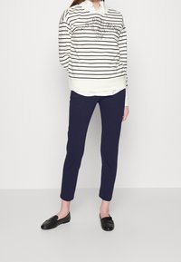 Vit- och marinrandig sweatshirt med logografik, kombinerad med marinbyxor och svarta loafers. Slät tyg, avslappnad passform och långa ärmar.