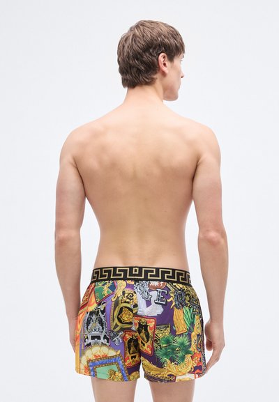 Χρωματιστά μαγιό βερμούδα με μαύρη μέση με σχέδια, που περιλαμβάνει διάφορα γραφικά σε κίτρινο, μωβ και πράσινο. Το υλικό φαίνεται ελαφρύ.