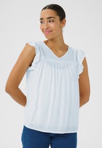 Haut bleu clair à manches courtes avec des bords volants, un col en V et un tissu texturé. Détails en dentelle décorative au niveau de la poitrine.
