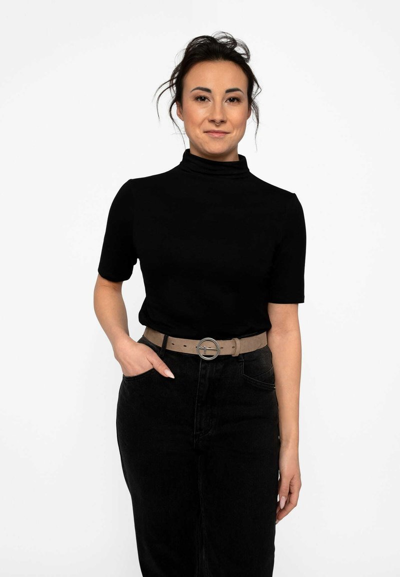 Haut noir à col roulé à manches courtes associé à un jean noir taille haute et une ceinture beige avec une boucle circulaire en argent.