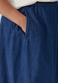 Dunkelblaue Jeansrock mit elastischem Bund, Seitentaschen und weicher Textur. Sichtbare Nahtdetails auf dem Stoff.