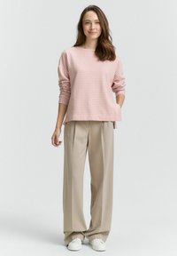 Maglietta a maniche lunghe a righe rosa chiaro abbinata a pantaloni beige a gamba larga e sneaker bianche. La maglietta presenta una vestibilità comoda e spacchi laterali.
