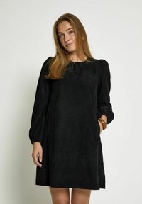 Black corduroy dress with long puff sleeves, round neckline, and side pockets. Ribbed texture, above-knee length, and loose fit.