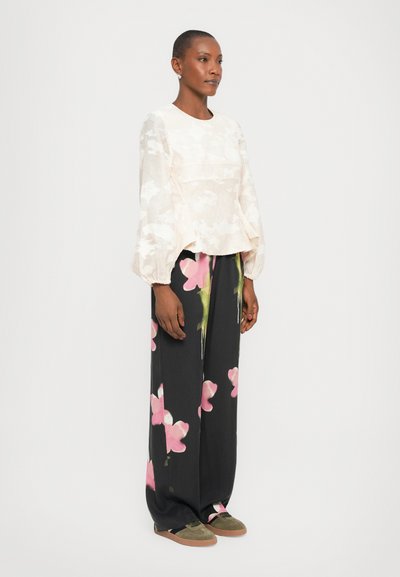 Lichtbeige, getextureerde blouse met lange, puffende mouwen, gecombineerd met zwarte broek met wijde pijpen en grote roze bloemenprint met groene accenten.