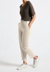 Ljust beige linnebyxor med två framfickor, knappstängning och avslappnad passform, tillsammans med en mörkbrun kortärmad stickad topp och vita sneakers.