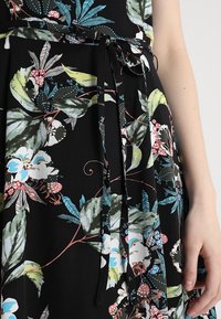Vestido de tela negra con patrones coloridos de flores y hojas, cintura ajustada con un lazo y una textura suave.