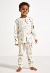Kremowe piżamy dziecięce wykonane z miękkiego materiału, z niebieskimi ilustracjami postaci, chmur i gwiazd na bluzce i spodniach.