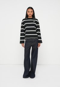 T-shirt à manches longues rayé noir et blanc avec un col rond ; assorti à un jean large bleu foncé ; coupe décontractée et design minimaliste.