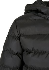 Schwarze Steppjacke von hinten mit horizontalen Nähten und einem oben sichtbaren, erhöhten, gepolsterten Kragen.
