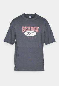 T-shirt en coton gris foncé à manches courtes et col rond, avec un logo rouge "REEBOK" et le texte "CLASSIC" dans un design ovale blanc.