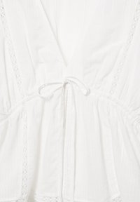 Biely ľahký top z látky s výstrihom do V, čipkované detaily, pružný pás a tenká šnúrka vpredu v strede.