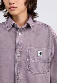 Svetlo sivkast jeans srajca s srebrnimi gumbi, s koničastim ovratnikom in žepom na prsih, ki ima značko z logotipom. Teksturna tkanina z zbledelim vzorcem.