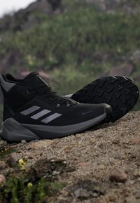 Czarne buty trekkingowe z szarymi akcentami, teksturowana gumowa podeszwa, wysoka konstrukcja oraz odblaskowe paski, wykonane z materiału wodoodpornego.