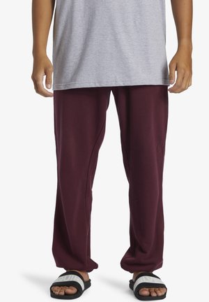 Maroon sweatpants with a relaxed fit, made from soft fabric, paired with black slide sandals featuring white accents. Gray t-shirt above.