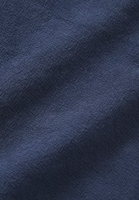 Blauw textiel met een dichtgeweven structuur en een subtiel reliëf van diamantvormige patronen, met zachte plooien en schaduwen.