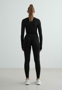Musta urheilu toppi ja korkeavyötäröiset leggingsit, joissa on sileä kangas. Asusteessa on tiukka muotoilu ja pitkät hihat, jotka on yhdistetty valkoisiin tennareihin.