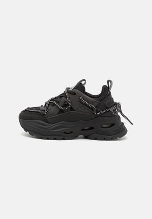 Kraftig sort sneaker med tyk sål, mesh- og læderpaneler, reflekterende tykke snørebånd samt trækflapper ved tungen og hælen.