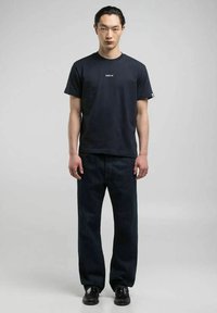 T-shirt in cotone navy con logo REPLAY, abbinato a jeans blu scuro a gamba dritta e scarpe nere. Modello in piedi davanti a uno sfondo neutro.