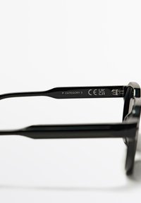 Schwarze Sonnenbrille mit dickem Kunststoffrahmen, geraden Bügeln und eingravierten Markierungen, darunter "P KATEGORIE 3" und Zertifizierungssymbole.