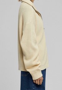 Krémový pletený svetr na zapínání s uvolněným střihem, límcem, dlouhými rukávy, žebrovanými manžetami a strukturovaným povrchem.