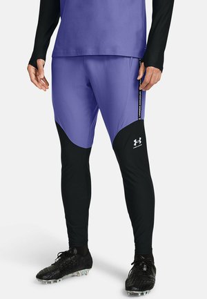 Paarse sportbroek met zwarte onderbenen, gemaakt van rekbaar materiaal. Bevat een logo op de bovenbeen en zijdetails in het wit.