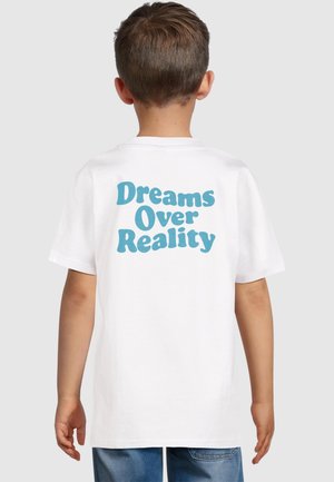 Camiseta de algodón blanco con gran texto azul en la parte posterior que dice "Los sueños sobre la realidad." Cuello redondo y mangas cortas. Ajuste casual.