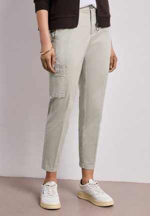 Kobieta nosząca jasnoszare spodnie typu cargo z boczną kieszenią, białe sneakersy i ciemnobrązowy sweter na zamek.