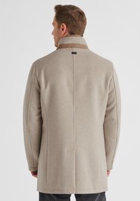 Beige Wollmischmantel mit geradem Schnitt, kontrastierendem braunen Kragen und minimalistischem Design. Beachten Sie die Rückennaht und die glatte Textur.