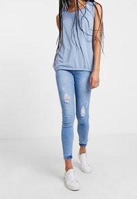 Ljusblå ärmlös topp med små vita prickar, i kombination med slitna ljusblå skinny jeans och vita sneakers.