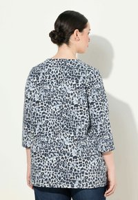 Bluzka w panterkę w jasnoniebieskim i granatowym kolorze, z rękawami 3/4 i okrągłym dekoltem. Miękki materiał o luźnym kroju i zaokrąglonym hemie.