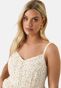 Kwiatowa sukienka na cienkich ramiączkach, z jasnym kremowym tłem, delikatnym nadrukiem w kolorze brzoskwiniowym i zielonym oraz guzikami wzdłuż środka.