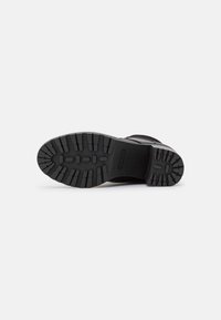 Suela de bota negra con un patrón de tracción robusto, con un tacón y paneles laterales lisos, fabricada con materiales sintéticos y goma duradera.