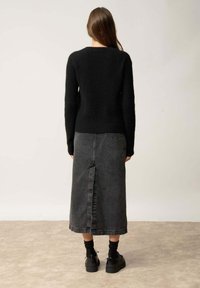 Pull en maille noir à texture côtelée associé à une jupe maxi en jean foncé avec une fente centrale au dos. Des chaussures noires à lacets viennent compléter le look.