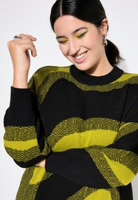 Maglione a maglia a righe nere e gialle con scollo rotondo, caratterizzato da disegni a forma di onda e polsini a costine. Tessuto morbido e vestibilità rilassata.