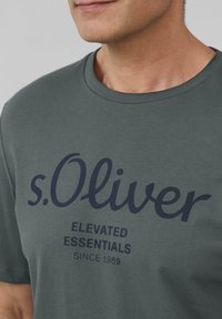 Zielona bawełniana koszulka z krótkim rękawem z nazwą marki "s.Oliver" w ciemnoniebieskim kolorze. Okrągły dekolt, krótkie rękawy i luźny krój.