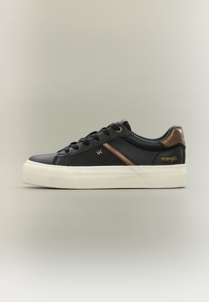 Baskets basses noires avec semelle blanche, accents bronze, lacets noirs et logo Wrangler sur le côté et sur la languette du talon.