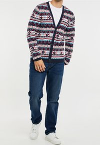Navy cardigan with colorful geometric patterns, featuring a V-neckline, buttons down the front, and ribbed cuffs and hem. Worn with blue jeans.