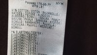 Ruhacímke, amely több nyelven mutatja a szövet összetételét, megnevezve a pamutot és az elasztomultiesztert a megfelelő százalékokkal.