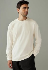 Cream long-sleeve t-shirt made of soft cotton, featuring a round neckline and relaxed fit, paired with black pants. Smooth texture.