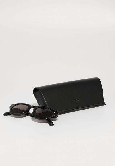 Black sunglasses with a vintage shape, featuring dark lenses and textured arms, alongside a sleek black hard case embossed with a logo.