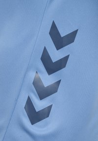 Niebieska tkanina z czterema ciemnoniebieskimi, skierowanymi w dół kształtami w jodełkę, ułożonymi pionowo, obok szwu po lewej stronie.