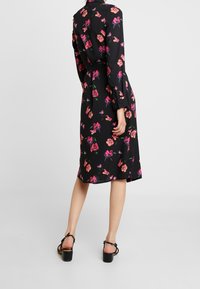 Robe noire florale à manches longues, taille ceinturée, longueur genoux, motifs de pivoine colorés, tissu doux et dos ouvert.