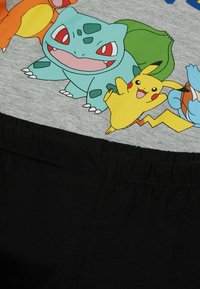Graues T-Shirt mit bunten Pokémon-Charakteren, darunter Bisasam, Pikachu und Glumanda. Schwarzer Stoff am unteren Ende mit elastischem Bund.