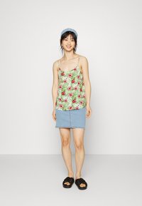 Top de tanque floral com padrões verdes e cor-de-rosa, combinado com uma saia de denim azul clara e sandálias de slide pretas. Alças e design casual.