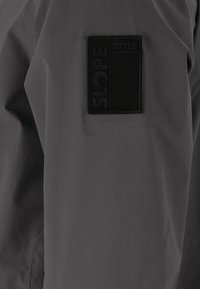 Harmaa vedenpitävä takki, jossa on teksturoitu SLOPE STYLE -merkki rinnassa. Materiaali vaikuttaa sileältä ja siinä on matta pinta.