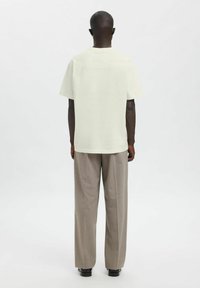 Lysebeige kortærmet t-shirt, set bagfra, med diskret tekst og branding, kombineret med lysegrå bukser med vide ben og sorte sko.