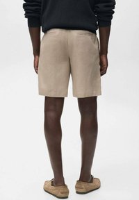 Pantalones cortos de lino beige con bolsillos traseros, combinados con un suéter negro y zapatos tipo mocasín marrones, vistos desde la parte trasera. Textura suave.