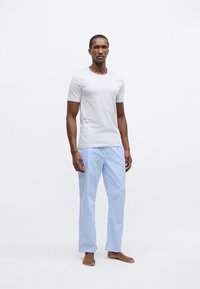 Svetlo siva majica kratkih rokavov, kombinirana z modro-belim karo pižamnim hlačami. Tkanina je videti gladka z udobnim, sproščenim krojem.