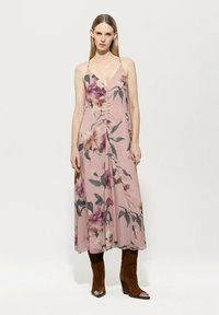 Rosa floral Maxi-Kleid mit V-Ausschnitt, gerafftem Vorderteil und verstellbaren Trägern, kombiniert mit braunen Stiefeln mit Absatz.