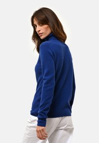 Niebieski sweter z golfem, uszyty z miękkiej, teksturowanej tkaniny, z długimi rękawami i dopasowanym krojem. Noszony z jasnymi spodniami.